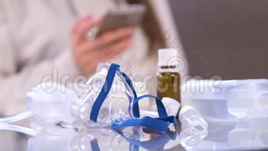 准备吸入。 <strong>雾化</strong>器，口罩和药品放在玻璃桌上.. 无法辨认的女人带着手机。